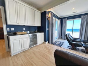 A kitchen with white cabinets, a refrigerator, and a view of the beach through large windows.