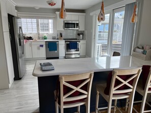 Cocina moderna con armarios blancos, electrodomésticos de acero inoxidable y una isla central con taburetes de bar.