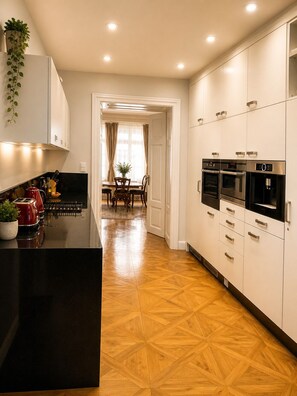 Une cuisine moderne avec un plan de travail noir, des appareils en acier inoxydable et un parquet en bois disposé en motif chevrons.