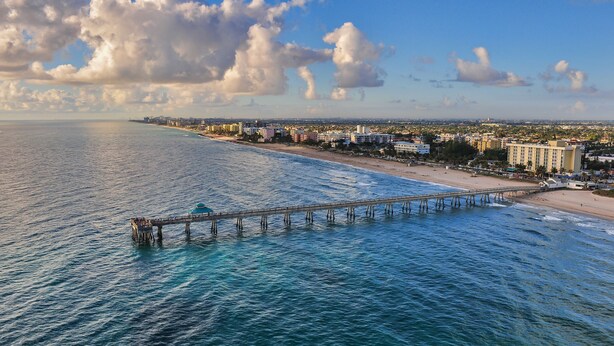 Eine Küstenstadt mit einem markanten Steg, der sich ins Meer erstreckt, einem Strand und einer Skyline aus Gebäuden.