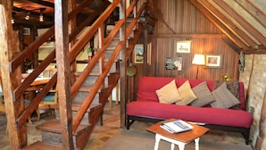 Habitació acollidora amb un sofà vermell, una escala de fusta i una taula petita amb un llibre.