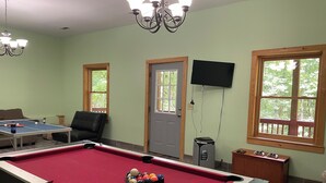 A pool table with balls, a television mounted on the wall, and a door with windows.