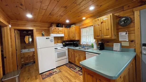 A wooden cabin interior with a kitchen area, including a refrigerator, stove, sink, and wooden cabinets.