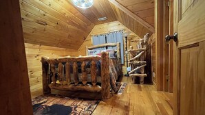 A log cabin interior with a wooden bed, a staircase, and a door.