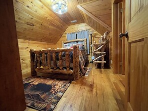 A log cabin interior with a wooden bed, a staircase, and a door.