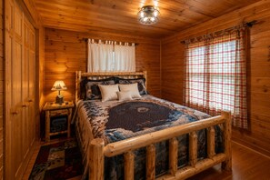 Une chambre à coucher dans un chalet en bois, avec un lit, une table de chevet, une lampe et une fenêtre ornée de rideaux à carreaux.