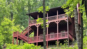 A multi-level wooden cabin with a staircase, surrounded by dense forest.