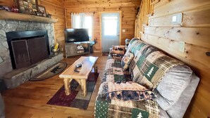 A wooden cabin interior with a stone fireplace, a television, a sofa, and a coffee table.