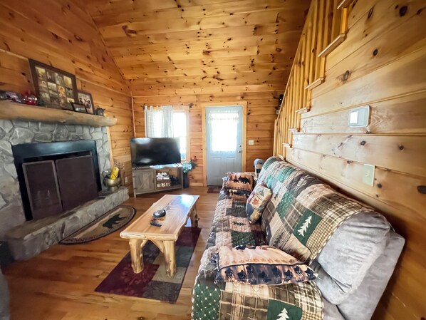 A wooden cabin interior with a stone fireplace, a television, a sofa, and a coffee table.