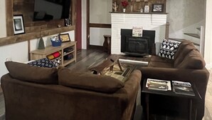 A living room with a brown sofa, a coffee table, a TV mounted on a wooden wall, and a fireplace with a mantel. - Newly Renovated Country Home Located near Greenbrier River (Alderson)