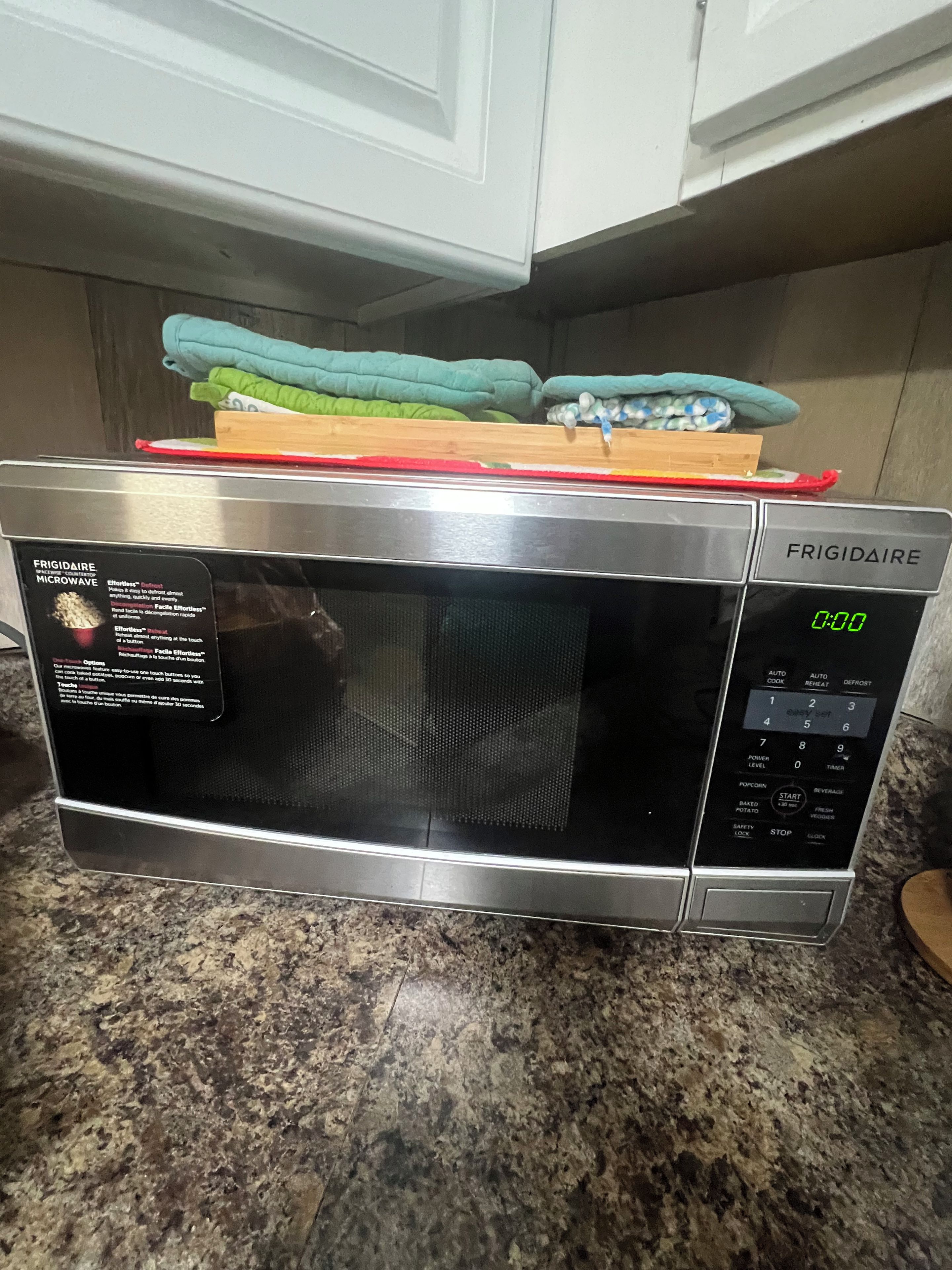 Une cuisine équipée d’un four à micro-ondes Frigidaire en acier inoxydable, posé sur un plan de travail en granit.