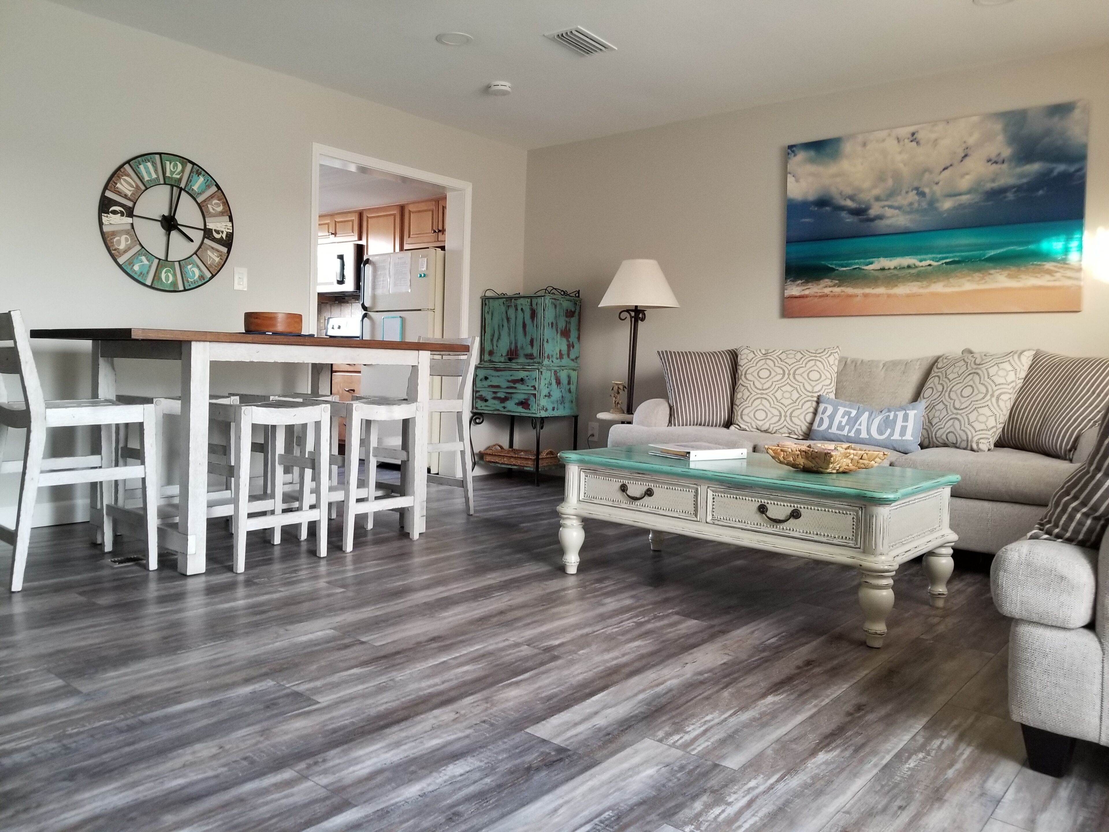 A living room with a dining area, a teal cabinet, and a beach-themed painting.