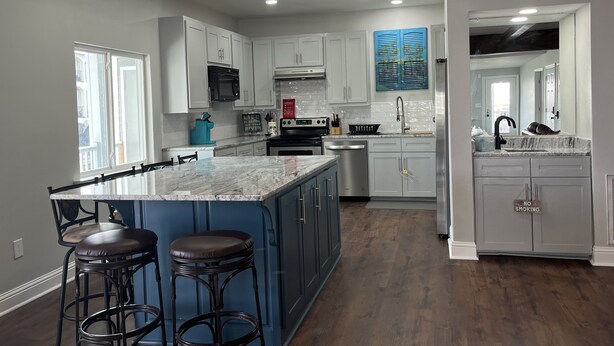 A modern kitchen with white cabinets, a blue island with stools, stainless steel appliances, and a 'No Smoking' sign. - Louisiana Tickfaw River House Near New Orleans, Baton Rouge! Best Views! HotTub! (Springfield)
