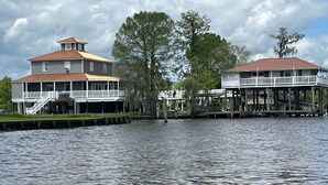 A waterfront property with two large buildings, one with a balcony and the other with a covered deck. - Louisiana Tickfaw River House Near New Orleans, Baton Rouge! Best Views! HotTub! (Springfield)