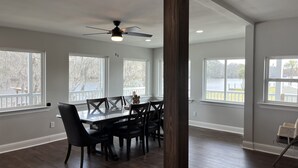 A spacious dining area with a large table and chairs, large windows with views of trees and a dock, and a ceiling fan. - Louisiana Tickfaw River House Near New Orleans, Baton Rouge! Best Views! HotTub! (Springfield)
