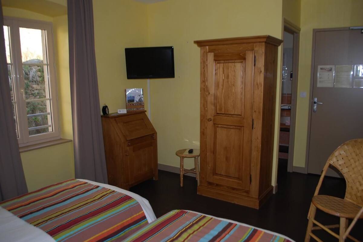 Une chambre avec deux lits, une armoire en bois, une télévision et un petit tabouret.