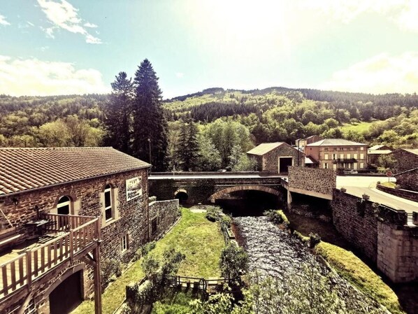 A historic stone building with a bridge over a stream, surrounded by lush greenery and hills. - Auberge de Chanteuges (Chanteuges)