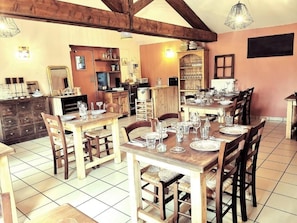 A dining area with wooden tables and chairs, a kitchen in the background, and a tiled floor. - Auberge de Chanteuges (Chanteuges)