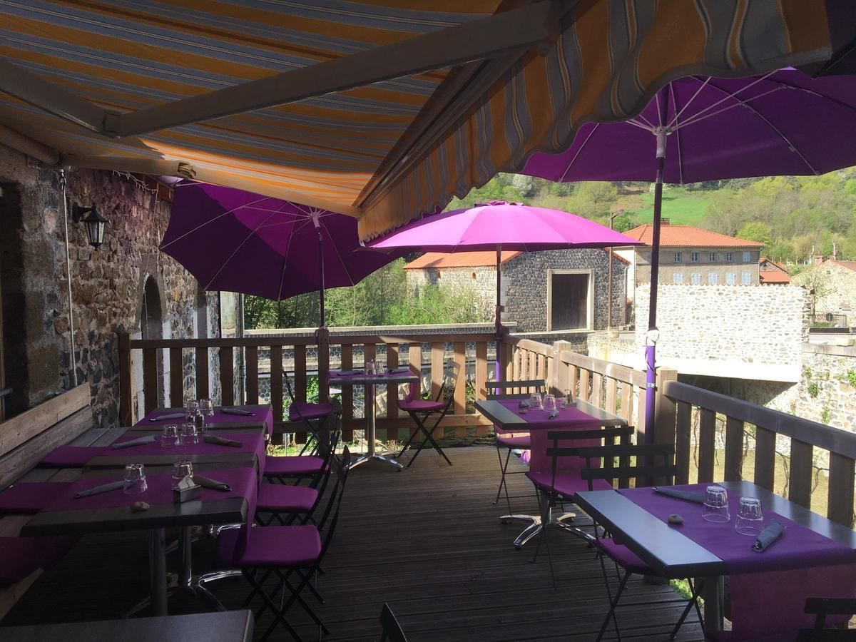 An outdoor dining area with tables and chairs, covered by striped awnings and purple umbrellas.
