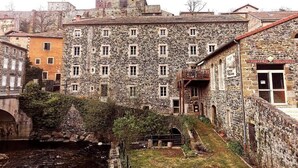 Um edifício de pedra com várias janelas e uma varanda, cercado por outros edifícios e uma pequena ponte.