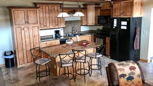 A kitchen with wooden cabinets, a granite countertop, a black refrigerator, and a bar area with stools.