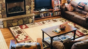 A cozy living room with a stone fireplace, a television, a bookshelf, a patterned rug, and a comfortable sofa.