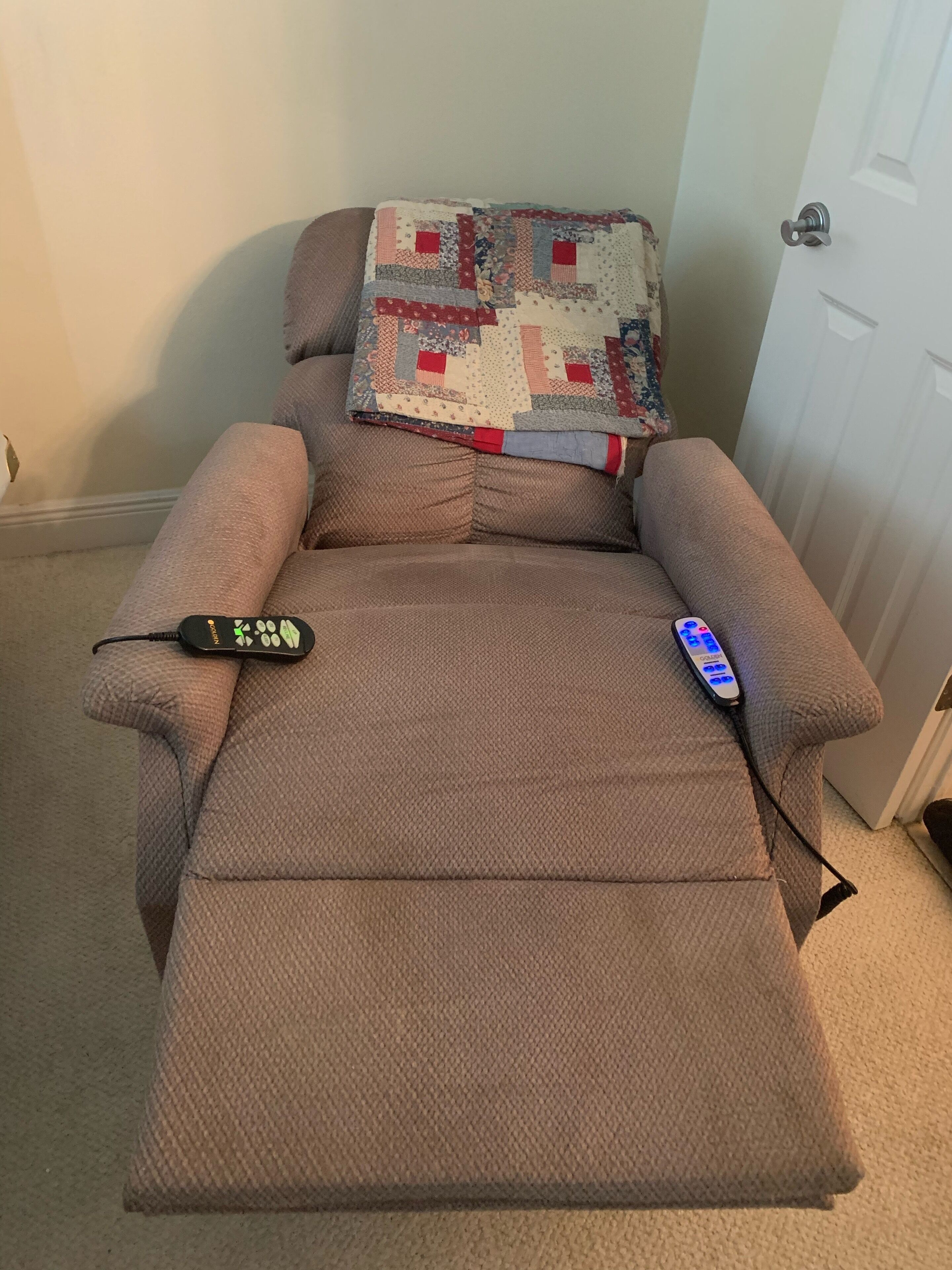 A recliner chair with a quilted blanket and a remote control on it.
