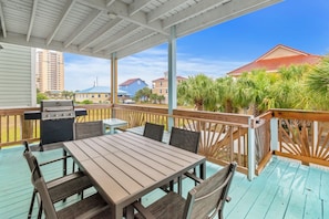 A covered outdoor patio with a table and chairs, a grill, and a view of surrounding buildings and palm trees. - Sunbeam-Soundview Private Home. 2 Min Walk to the Beach (Navarre)