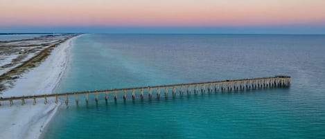 A pier extending into a calm sea with a beach on one side.