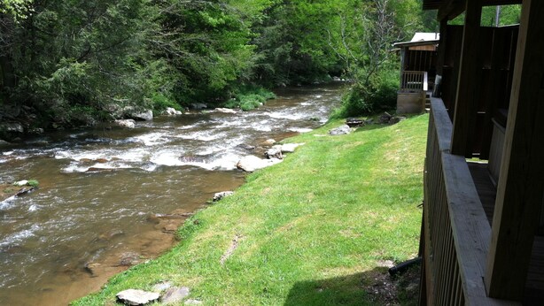 A river flowing through a wooded area with a wooden structure on the right.