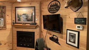 A cozy cabin interior with a fireplace, a mounted deer head, a television, and various framed pictures.