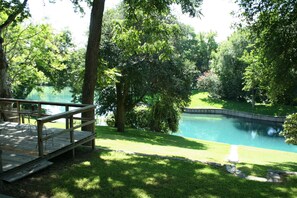 Um deck de madeira com móveis de exterior com vista para um lago rodeado por árvores.