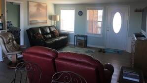A living room with a black leather sofa, a red chair, a wooden coffee table, and a ceiling fan. - Kayaker and Bird Watchers Dream: Freshly Renovated with Breathtaking Views (Cedar Point)