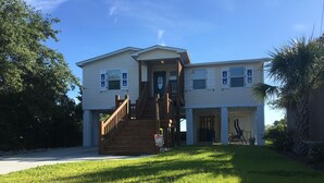 A two-story house with a wooden staircase leading to the front door, a covered porch, and a small garden area. - Kayaker and Bird Watchers Dream: Freshly Renovated with Breathtaking Views (Cedar Point)