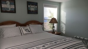 A neatly made bed with striped bedding and a decorative pillow, a wooden headboard, and two wall art pieces. - Kayaker and Bird Watchers Dream: Freshly Renovated with Breathtaking Views (Cedar Point)