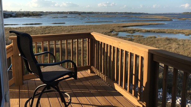 A wooden deck with a chair, overlooking a marshy landscape with water and distant buildings. - Kayaker and Bird Watchers Dream: Freshly Renovated with Breathtaking Views (Cedar Point)