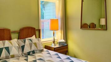 Une chambre d’hôtel avec un lit, une table de chevet, une lampe, une fenêtre avec des rideaux et un miroir au mur.