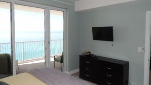 Une chambre à coucher comprenant un lit, une commode, un téléviseur et un balcon avec vue sur l’océan.