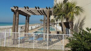 Une pergola en bois avec un espace piscine, une clôture blanche et une vue sur la plage et l’océan.