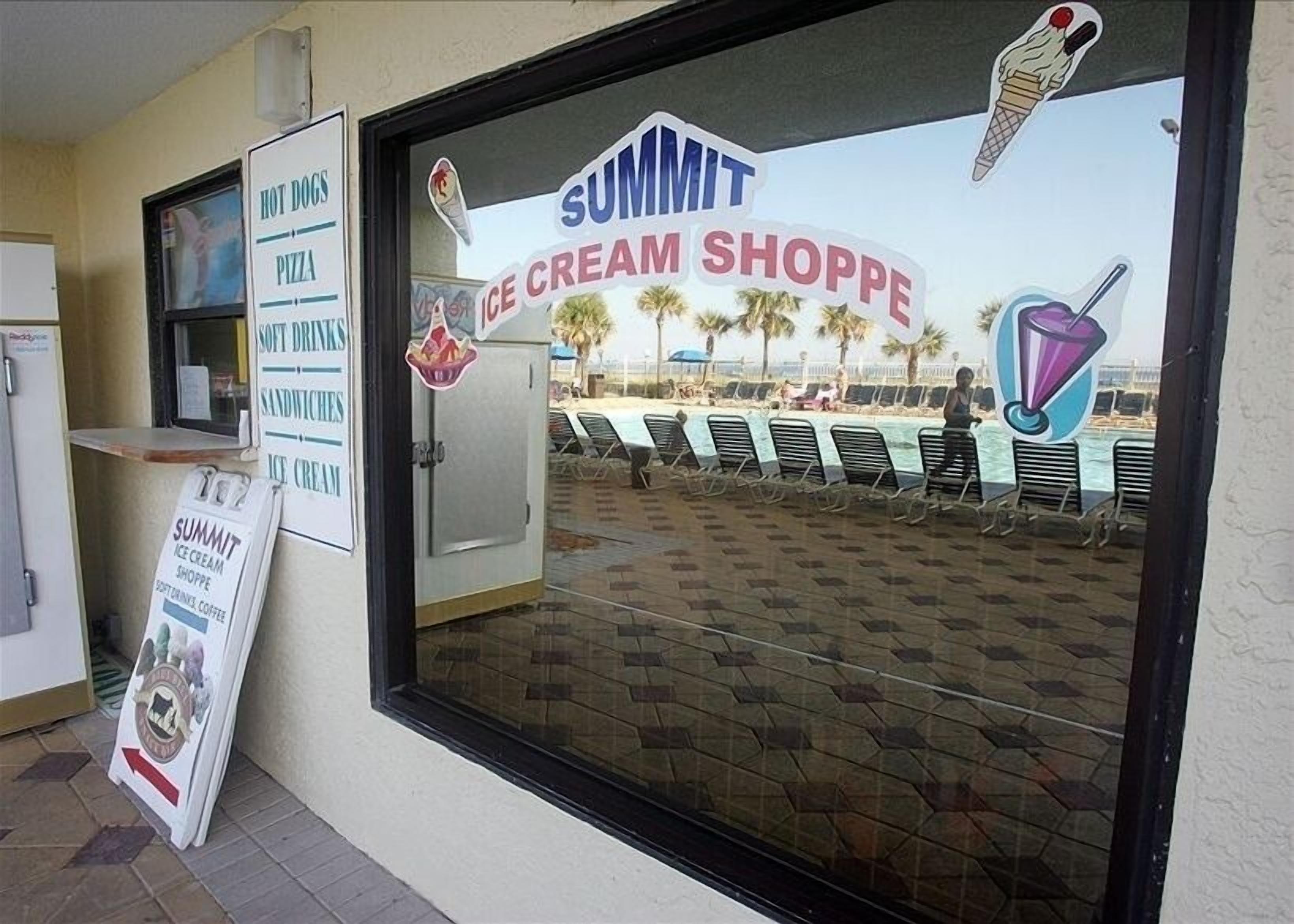 Een winkelgevel met een bord voor 'Summit Ice Cream Shoppe' en een menubord waarop onder meer hotdogs, pizza, frisdranken, sandwiches en ijs staan vermeld.