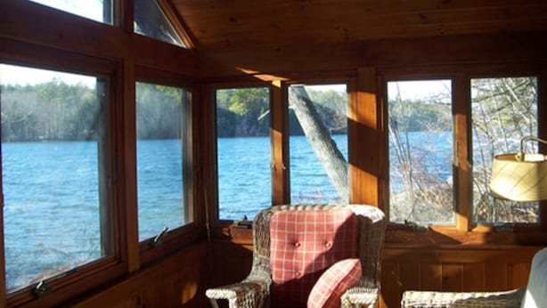 A cabin with large windows overlooking a lake, a wicker chair, and a lamp. - Lake Front Cabin on Squam Lake/On Golden Pond (Center Harbor)