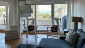 Une pièce spacieuse avec un escalier en colimaçon, un balcon offrant une vue sur la mer et un coin salon confortable avec un canapé et des fauteuils.