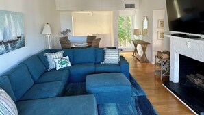 Un salon comprenant un canapé d’angle, une cheminée, un téléviseur et un coin repas avec des chaises en osier.
