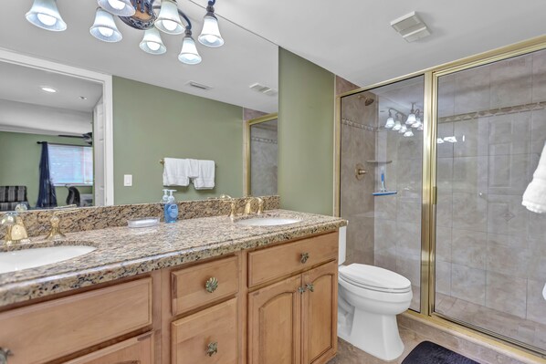 A bathroom with two sinks, a toilet, and a glass-enclosed shower. - 2BR Comfortable Condo with Easy Beach Access (Jupiter)