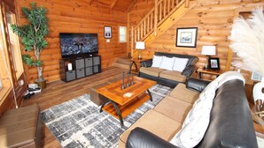 Ein Blockhaussalon mit einer Holztreppe, einem Fernseher, einem Sofa, einem Couchtisch und einem Topfpflanze.