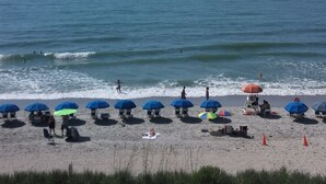 A beach with umbrellas and beach chairs, a lifeguard tower, and the ocean. - Myrtle Beach Oceanfront Condo. Sept. open Dates 79 a night. (Myrtle Beach)