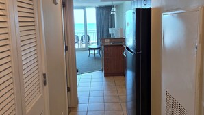 A corridor leading to a kitchen with a refrigerator, a dining area with a table and chairs, and a view of the ocean through a window. - Myrtle Beach Oceanfront Condo. Sept. open Dates 79 a night. (Myrtle Beach)