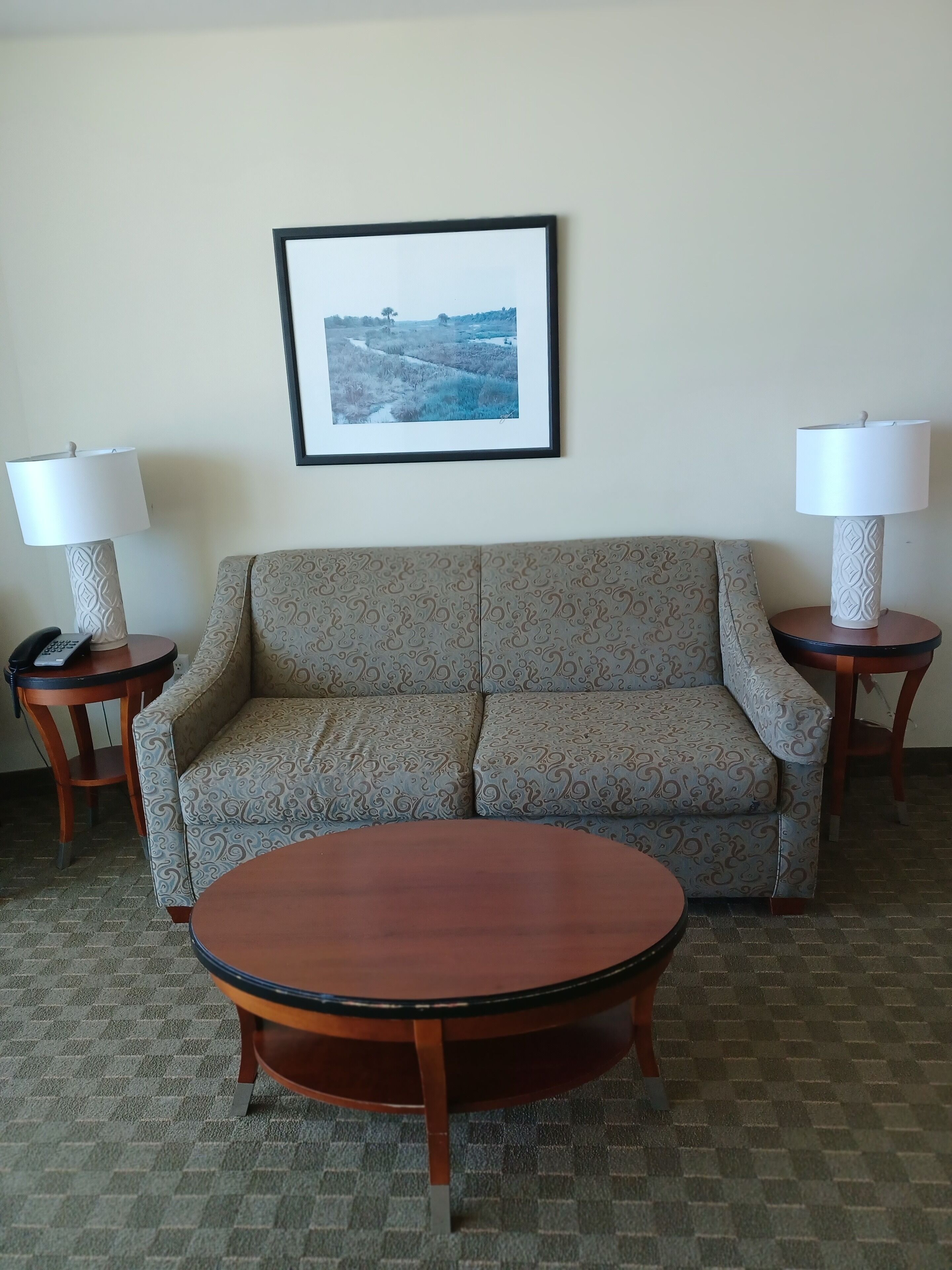 A living room with a sofa, two side tables with lamps, a framed picture on the wall, and a round coffee table.