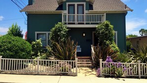 A two-story house with a front porch, a balcony, and a front yard with various plants. - Family Friendly 3BR Getaway! Central, Convenient, & Charming. (San Diego)