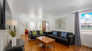 A modern living room with a black leather sofa, wooden coffee table, and a staircase leading to another level. - Family Friendly 3BR Getaway! Central, Convenient, & Charming. (San Diego)